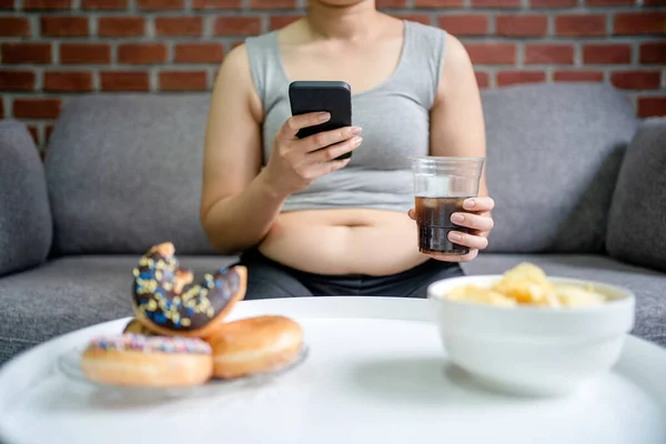 过度和贪婪的概念 肥胖妇女坐在沙发上吃着不健康的食物 — 图库照片