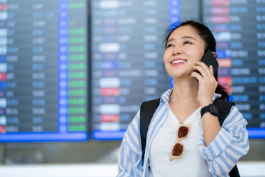 Akıllı telefonu kullanan Asyalı gezgin, havaalanındaki uçuş bilgi ekranına kayıt yaptırmak, seyahat etmek ve teknoloji konseptiyle ulaşımı sağlamak istiyor..