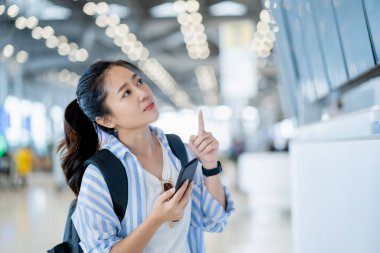 Genç Asyalı kadın gezgin havaalanı terminalinde akıllı telefon kontrol haritası ve uçuş çizelgesi kullanıyor. yeni normal seyahat, yaşam tarzı konsepti.