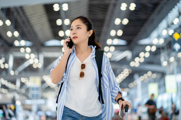 Young attractive asian female traveller are using smartphones device to make an appointment with a friend with luggage and handbag at airport terminal