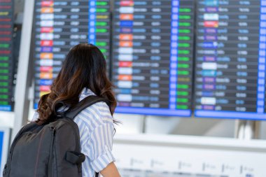 Woman tourist checking flight time table on board in airport. With copy space clipart