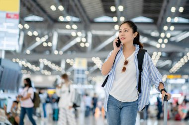 Asya 'lı kadın yolcu, uçağını beklerken cep telefonu kullanıyor ve terminalde bekliyor..