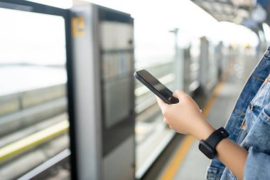 Platformda akıllı telefon kullanarak yakın plan çekimde gökyüzü treni ulaşımını bekliyoruz..