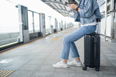 Kadın çantanın üzerinde oturuyor ve tren istasyonunda bekliyor..