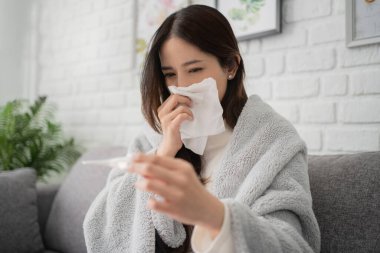 Hasta Asyalı kadın burnunu siliyor, öksürüyor, hapşırıyor ve evde vücut ısısını kontrol ediyor..