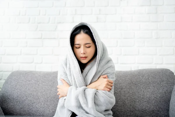 Close up sick asian woman covered with blanket sitting on couch, ill young female in warm suffering from fever, catch cold or flu, virus symptoms.