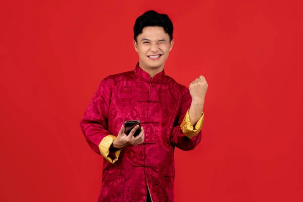 Young man asian happy smiling celebrate. While he using smartphone standing isolated on red background in studio.