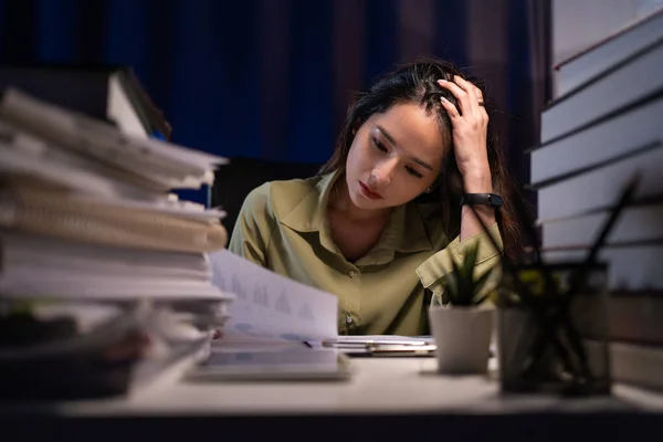 Asian businesswoman working hard late hours with a lot of document at home. She is busy and exhausted of work overtime at night.