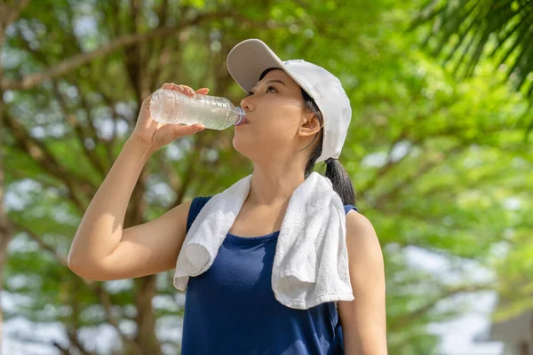 Happy woman drinking water after workout exercising at garden in the city at sunrise.