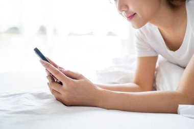 Rahat bir kadın sabah evde yatakta akıllı telefon kullanıyor.