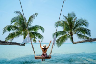 Deniz sahilinin tadını çıkaran bir kadın. Palmiye ağacının gölgesinde, tahta bir salıncakta oturuyordu. Seyahat kavramı.