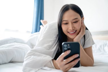 Heyecanlı Asyalı güzel bir kadın evinde yatağında cep telefonu kullanıyor.. 