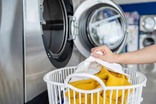 Woman picking up dirty clothes in a bin and putting them in the washing machine in a laundry shop