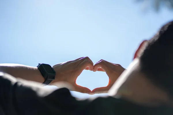 Male hands in the shape of a heart on the sky as background.