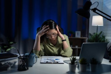 Asyalı iş kadını evde bir sürü belgeyle geç saatlere kadar çalışıyor. Geceleri fazla mesai yapmaktan yorulmuş..