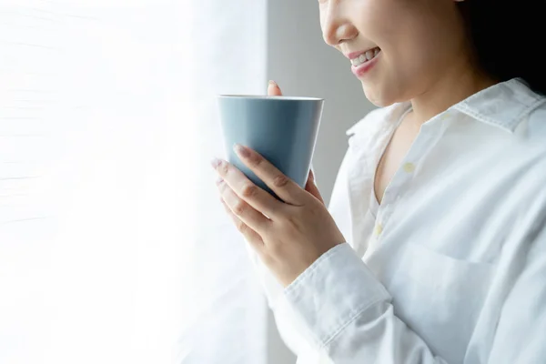 Stock image Closeup image of a beautiful young asian woman smelling and drinking coffee. She sitting near the window in the morning.