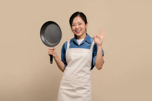 Mooie Aziatische Lachende Vrouw Schort Koekenpan Staand Geïsoleerd Lichtbruine Achtergrond — Stockfoto