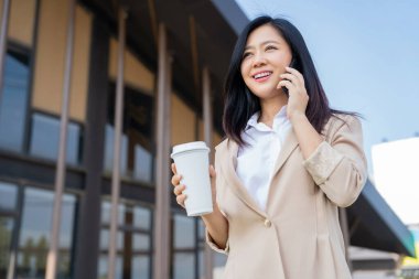 Şehirde yürürken cep telefonu kullanan neşeli Asyalı kadın.