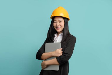 Siyah takım elbiseli ve kasklı güzel bir Asyalı mühendis elinde izole edilmiş bir tablet bilgisayar tutuyor..