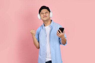 Başarılı bir Asyalı. Kablosuz kulaklık takan ve akıllı telefon kullanan yakışıklı bir genç. Pembe boş fotokopi stüdyosundan izole edilmiş..