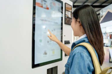 Kahve menüsünü otomattan seçen Asyalı kadın turist.