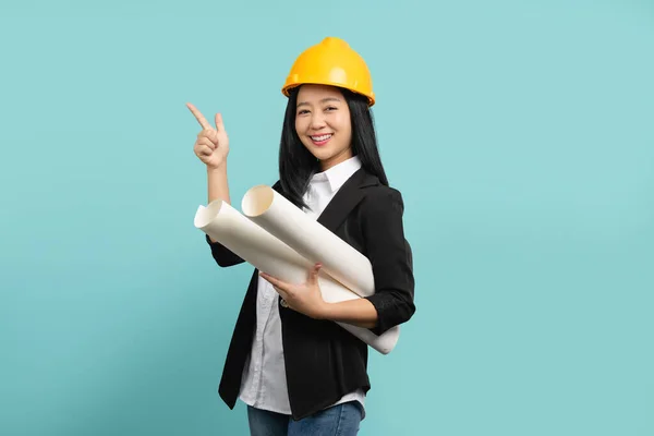 stock image Smiling professional asian female architect, engineer in safety helmet introduce construction project, pointing hand and carry blueprint