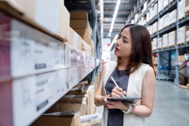 Güzel Asyalı yönetici dijital tablet tutuyor ve depodaki stokları kontrol ediyor.