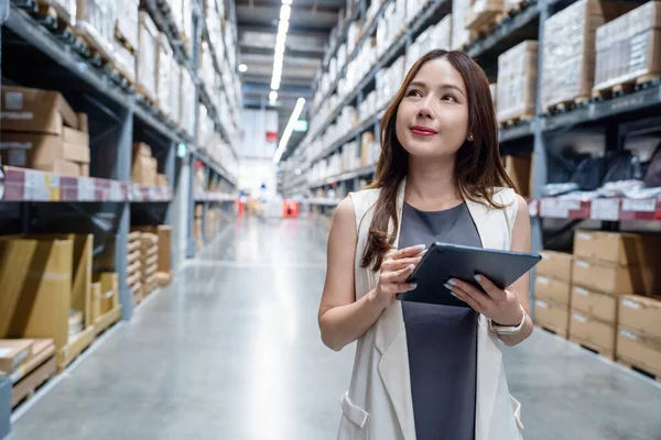 Asyalı kadın işyeri sahibi dağıtımı bekleyen bir depoda malları kontrol ediyor. Lojistik işleri, ulaşım hizmetleri ve lojistik dağıtımı.
