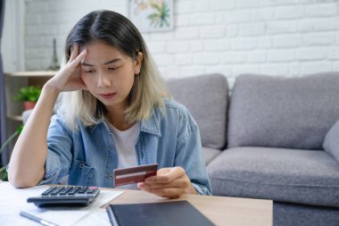 Young Asian woman with credit card debt. She felt stressed out after calculating bills or bills in her living room. clipart