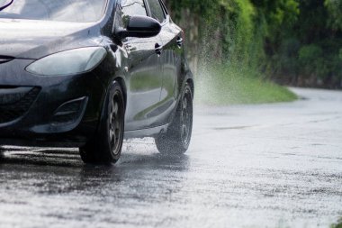 Su basmış caddedeki su birikintisinin içinden araba geçiyor. Hareket eden araba