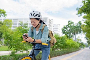 Genç Asyalı kadın parkta bisiklet üstünde akıllı telefon kullanıyor. teknoloji ve yaşam tarzı kavramı