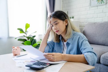 Oturma odasında hesap makinesi olan Asyalı kadın. Finansal hesapları olan ciddi bir kadın evdeki masanın üstündeki kağıt faturasına baktı..