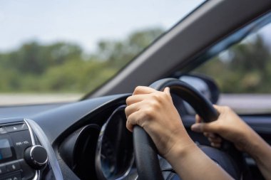 Female hands on the car steering wheel close up. Woman is driving a car. clipart