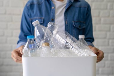 Bir sürü plastik şişeyle birlikte beyaz geri dönüşüm kutusunu tutan el fotoğrafı.