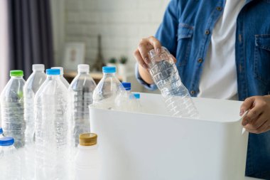 Elinde geri dönüşüm plastik şişesi olan bir kadın evdeki kağıt çöp kutusuna koyuyor.