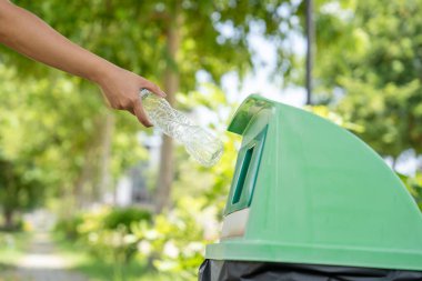 Kadın elleri plastik şişeleri yeşil çöp kutusuna atar..