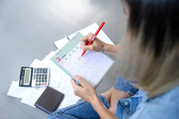 Asian woman sitting on floor home, stressed calculate expense from bills, She has no money to pay in mark circle deadline on calendar. Bankrupt person concept.