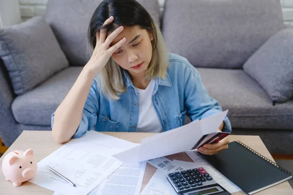 Young Asian woman is stressed because she looks at many expense bills and she has no money to pay credit card debt. She had a hand on her head, feeling very depressed.
