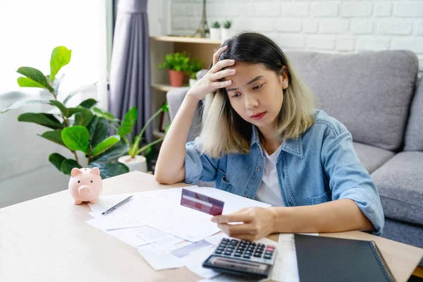 Stressed young asian woman with monthly bill expenses and credit card debt at home.