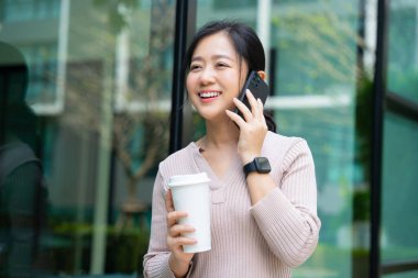 Arka planda kahve fincanıyla cep telefonuyla konuşan genç Asyalı kadın..