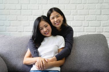 Mutlu lezbiyen LGBT Asyalı kız evdeki kanepede aşk ve romantizme sarılıyor..