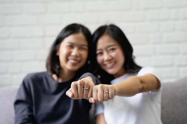 Young Asian couple is happy to show off their rings at home. Happy young Asian lesbian couple hugging each other in the living room at home.