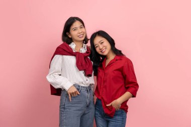 Çekici Asyalı kız arkadaşlar pembe arka planda birbirlerine sarılıyorlar..