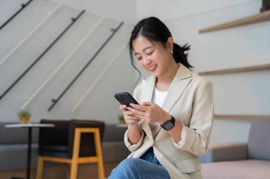 Akıllı, serbest çalışan Asyalı kadın koltukta akıllı telefon üzerinde çalışıyor. Her yerde mutlu çalışabilir..