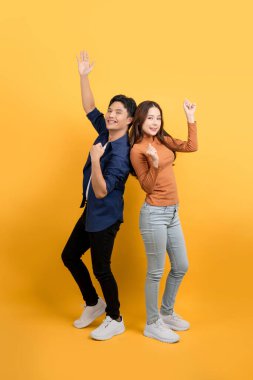Sırt sırta verip gülümseyen ve sarı izole edilmiş stüdyo arka planında yumruklarını sıkan neşeli Asyalı çiftin vücut görüntüsü..