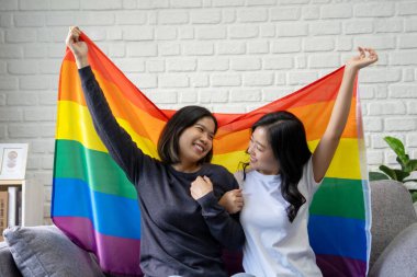LGBTQ Asyalı genç lezbiyen çift gülümseyerek gururlu bayrak mutluluğunu bir arada tutuyorlar..