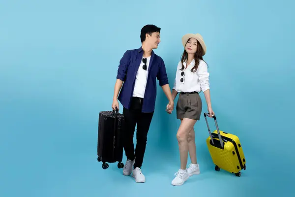 Happy Asian tourist in casual clothes holding a suitcase isolated on blue background. Tourists traveling abroad.