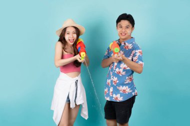 Suda plastik su tabancasıyla oynayan Asyalı bir turistin portresi. Mavi arka planda fotokopi alanı var. Songkran Festivali.