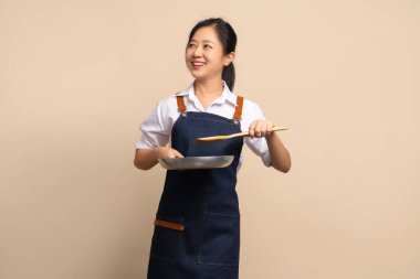 Önlük giyen güzel bir Asyalı kadın kahve dükkanı sahibi. Elinde bir tava ve fotokopi alanı olan ahşap bir spatula tutuyor..