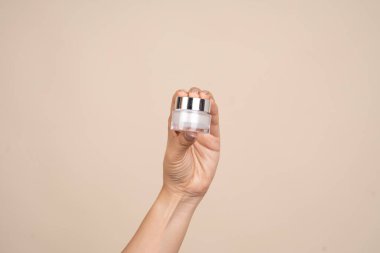 Kadının elinde krema kavanozu ve bej arka plan. Kozmetik ürünlerin reklam düzeni.